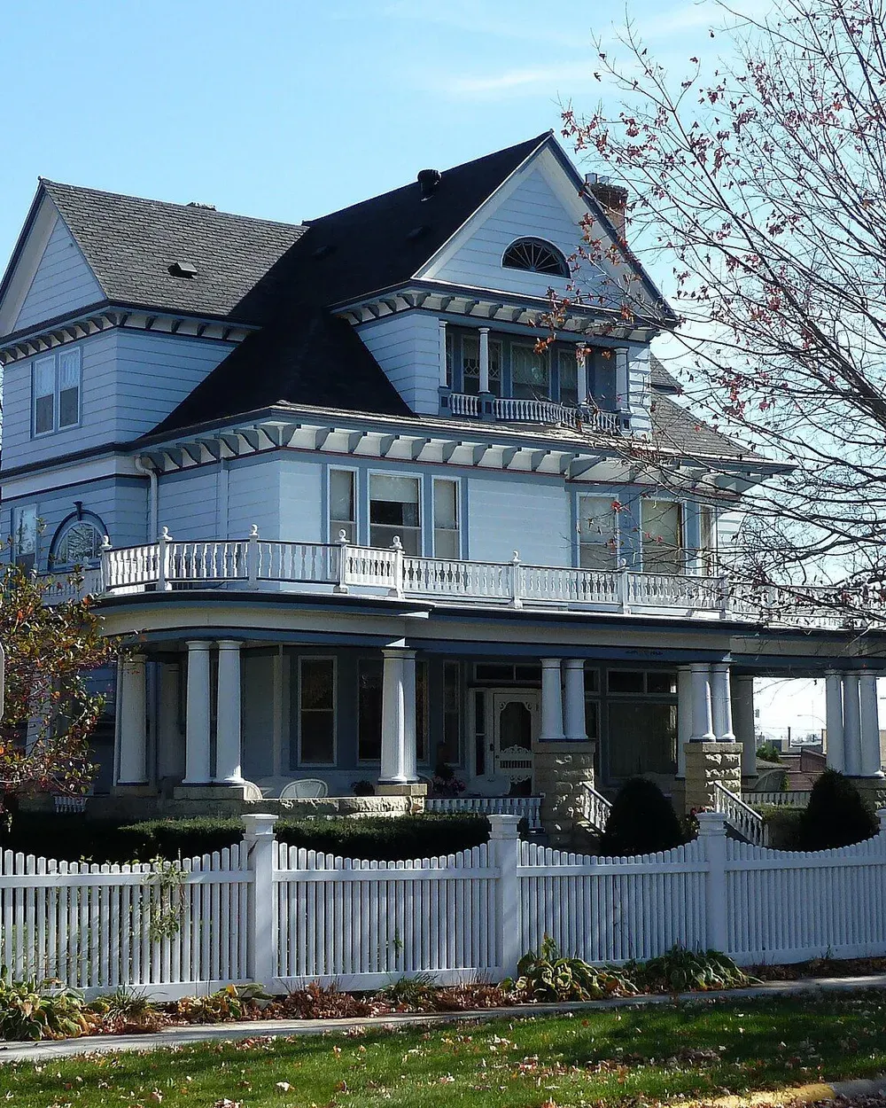 The Leuthold House, a Queen Anne Victorian home with a wraparound porch and white picket fence on a tree-lined street in Kasson, Minnesota.