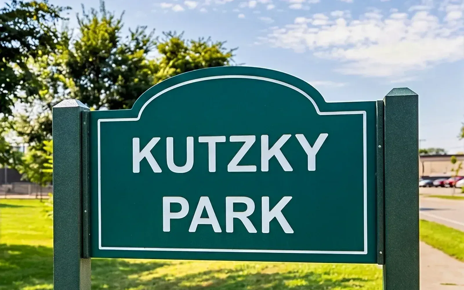 The Kutzky Park neighborhood sign in Rochester, Minnesota, set in the park lawn on a summer afternoon with mature trees in the background.