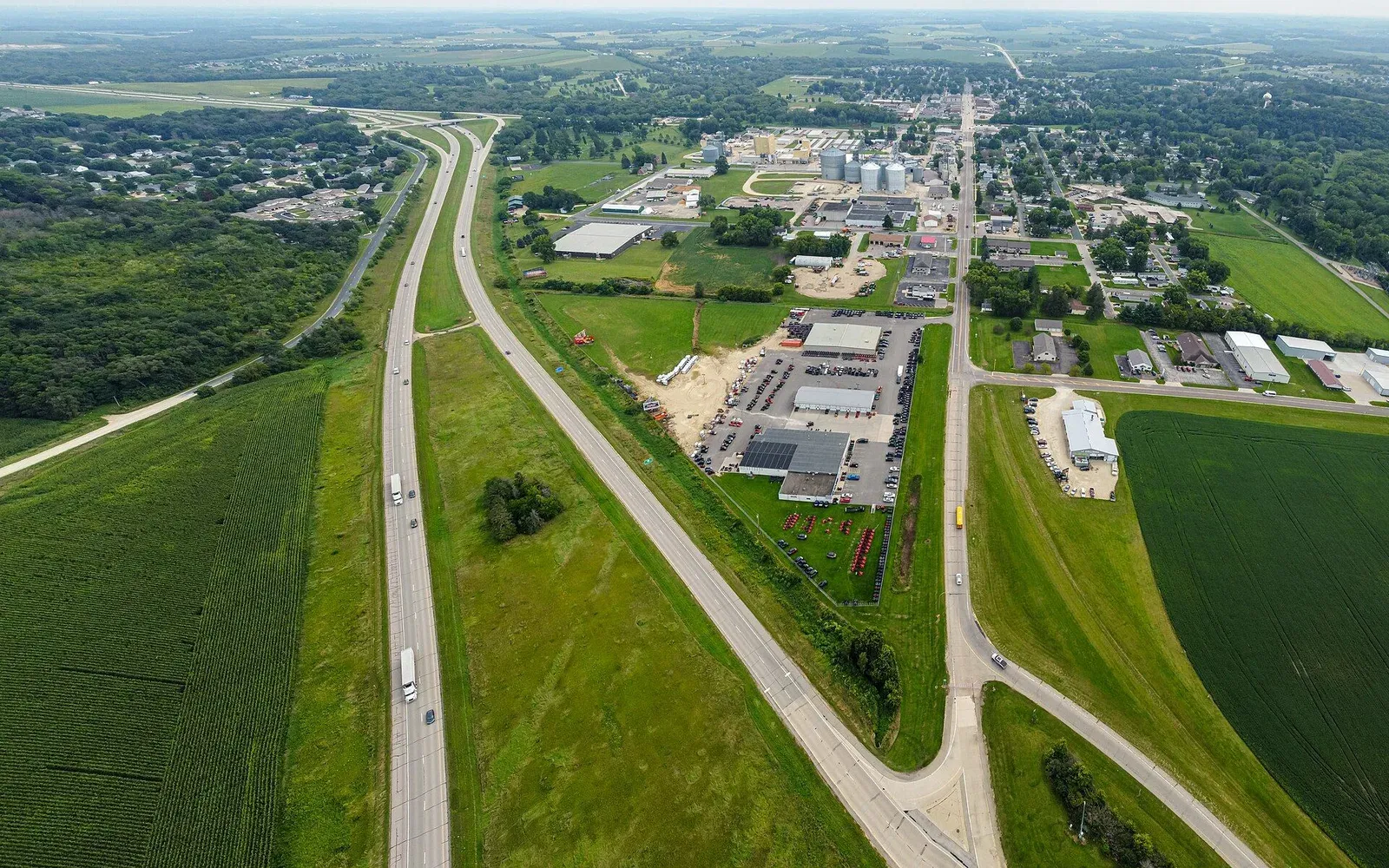 An aerial view of Pine Island, Minnesota, looking down the highway corridor toward town with farmland and commercial buildings flanking the road.